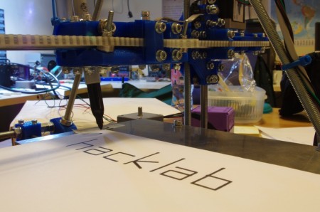 A RepRap machine writing "hacklab" with a pen