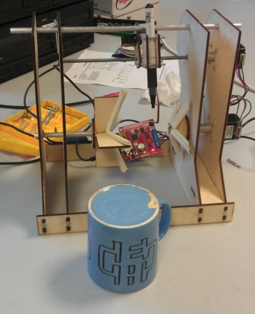 A completed not very good mug printer, standing next to a scruffy mug with the Edinburgh Hacklab logo scrawled on it, upside down.
