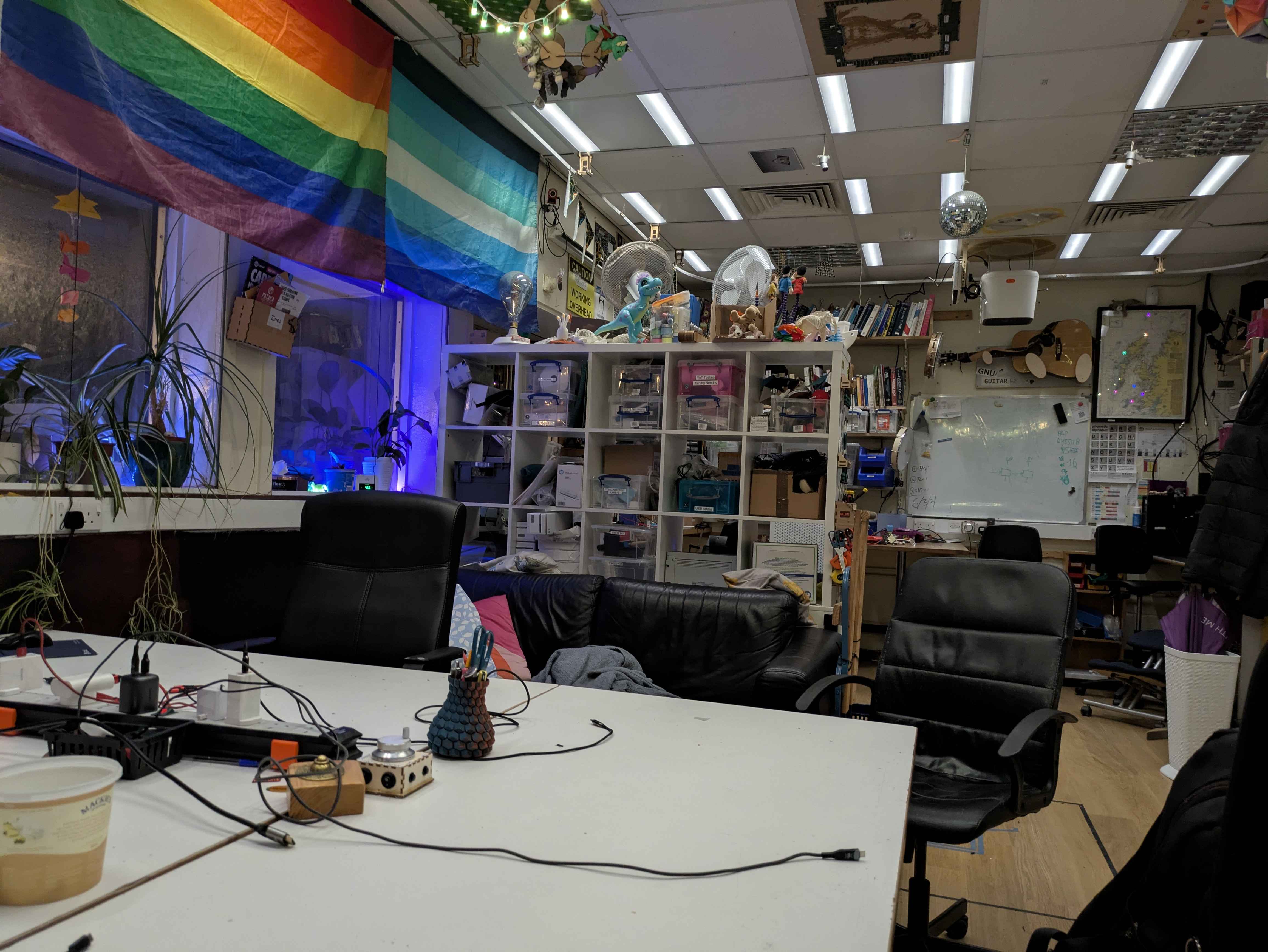 A busy-looking room with a desk, a bookshelf, some flags on the wall, and a whiteboard
