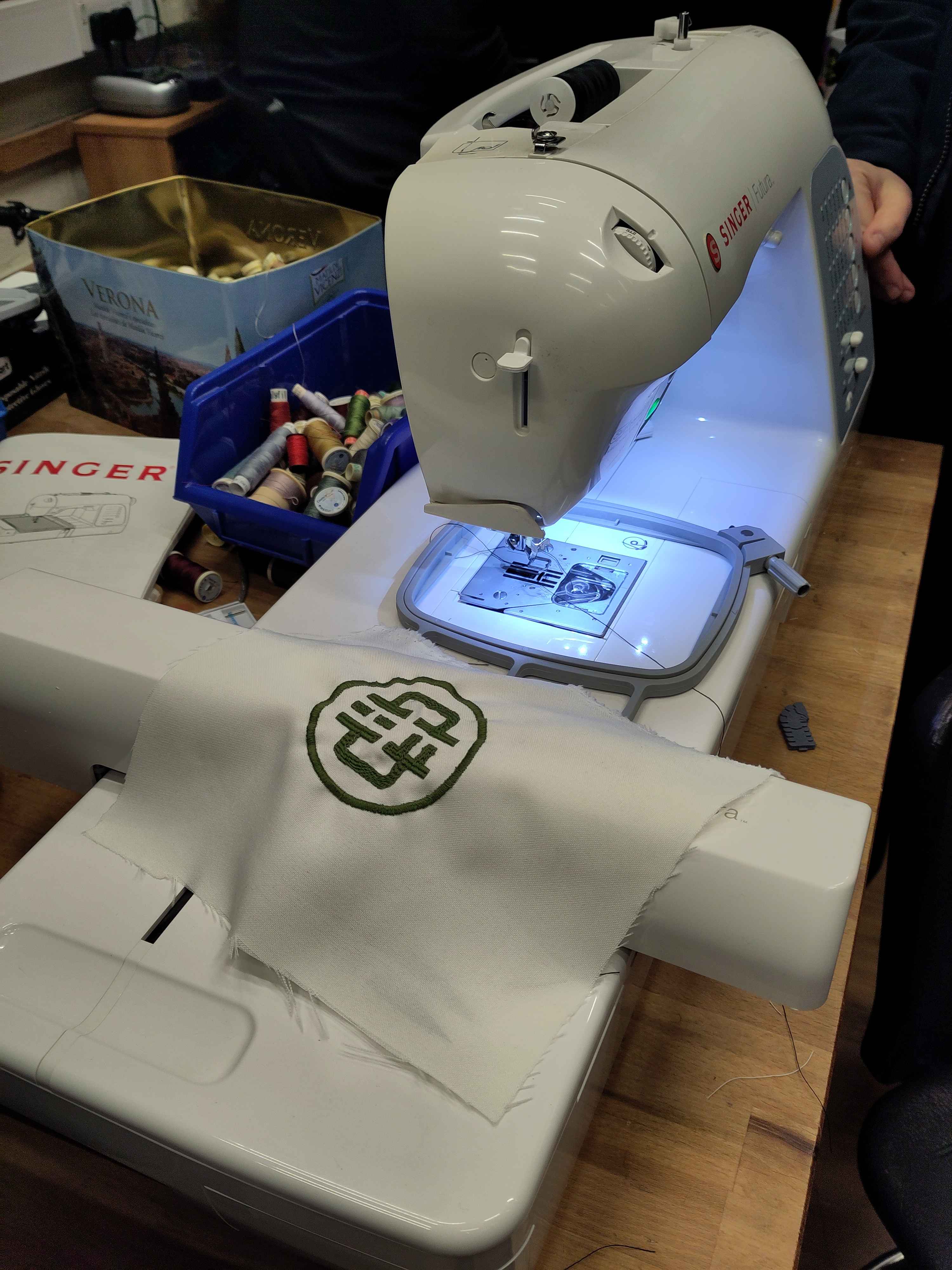 An embroidery machine, and a piece of fabric with the hacklab logo embroidered on it.