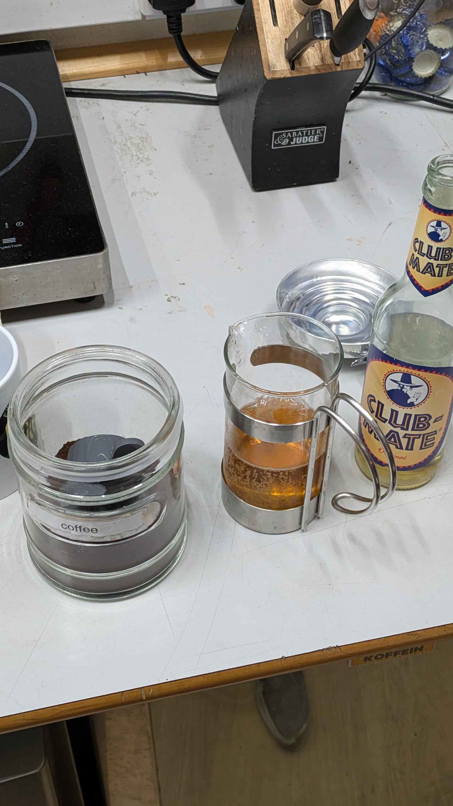 A container of coffee, a cafetiere, and a bottle of club mate